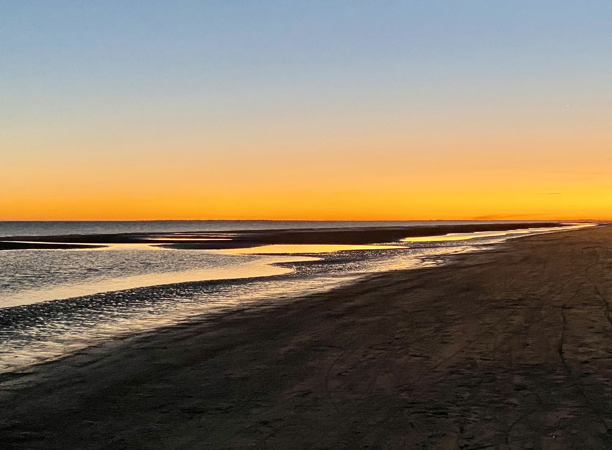 Sunset reflected on the wet sand at the water's edge.