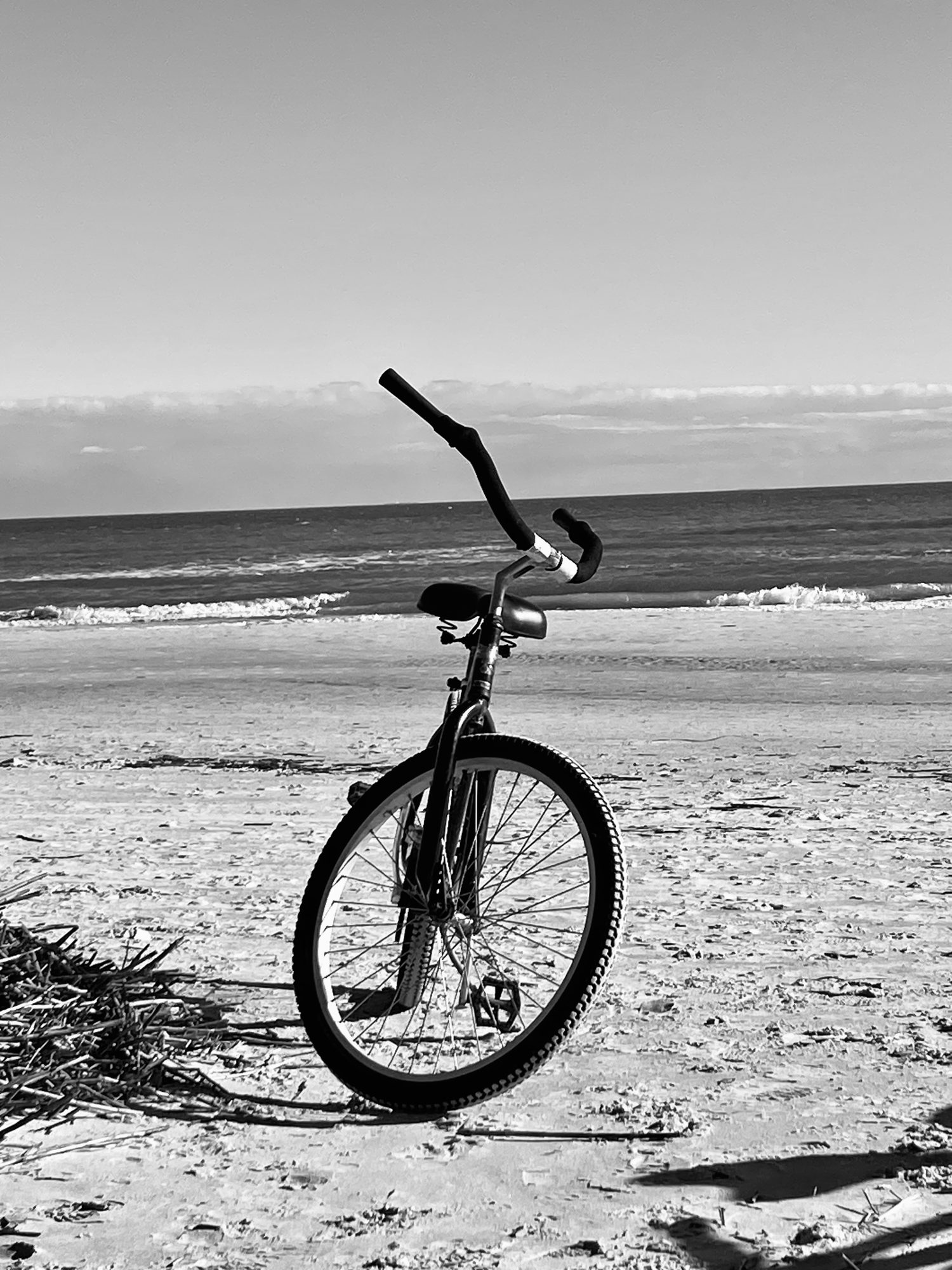 A bicycle on wet sand in black and white, waves behind it.