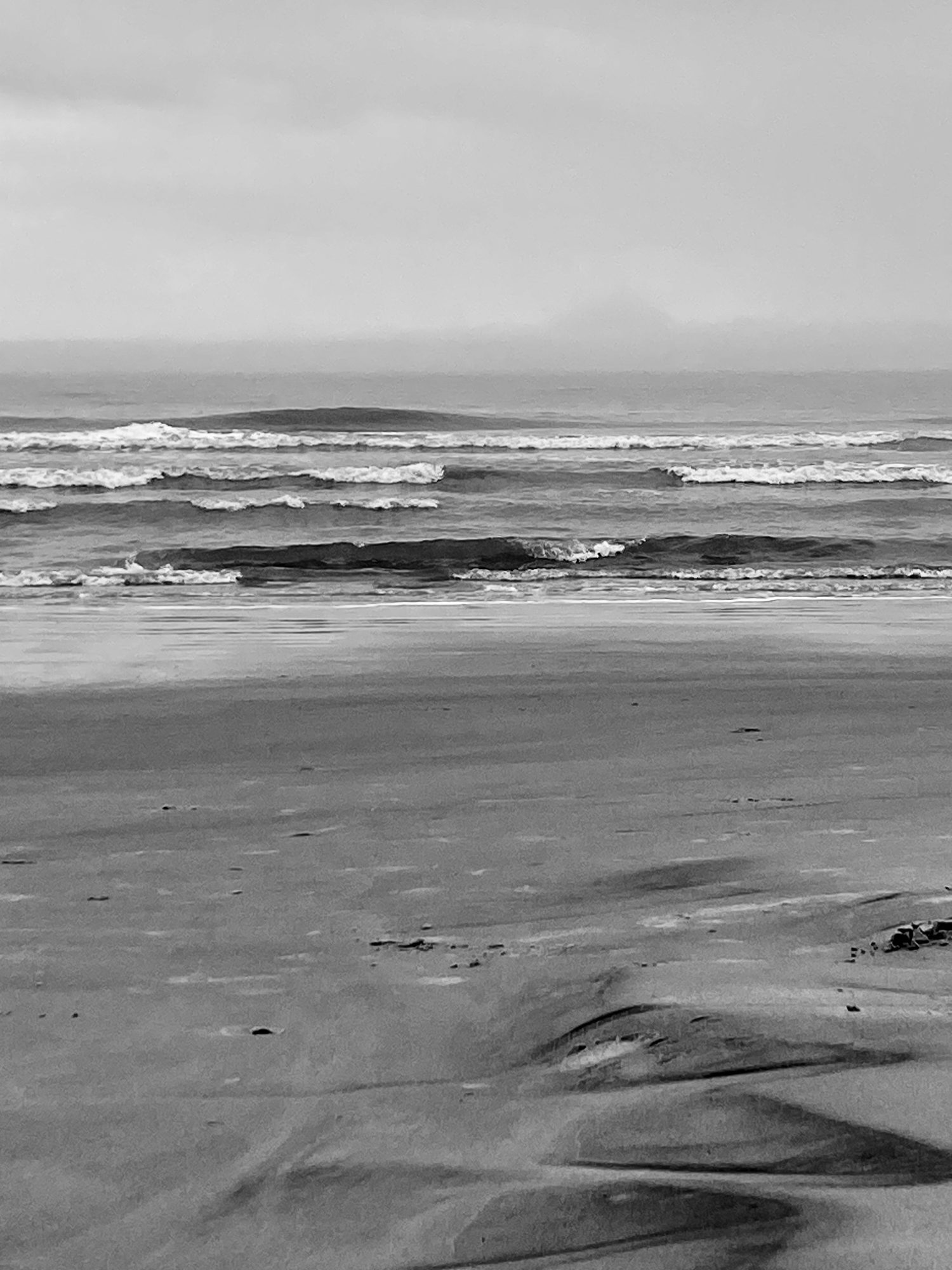 Coastal waves in black and white, sand and open sky.