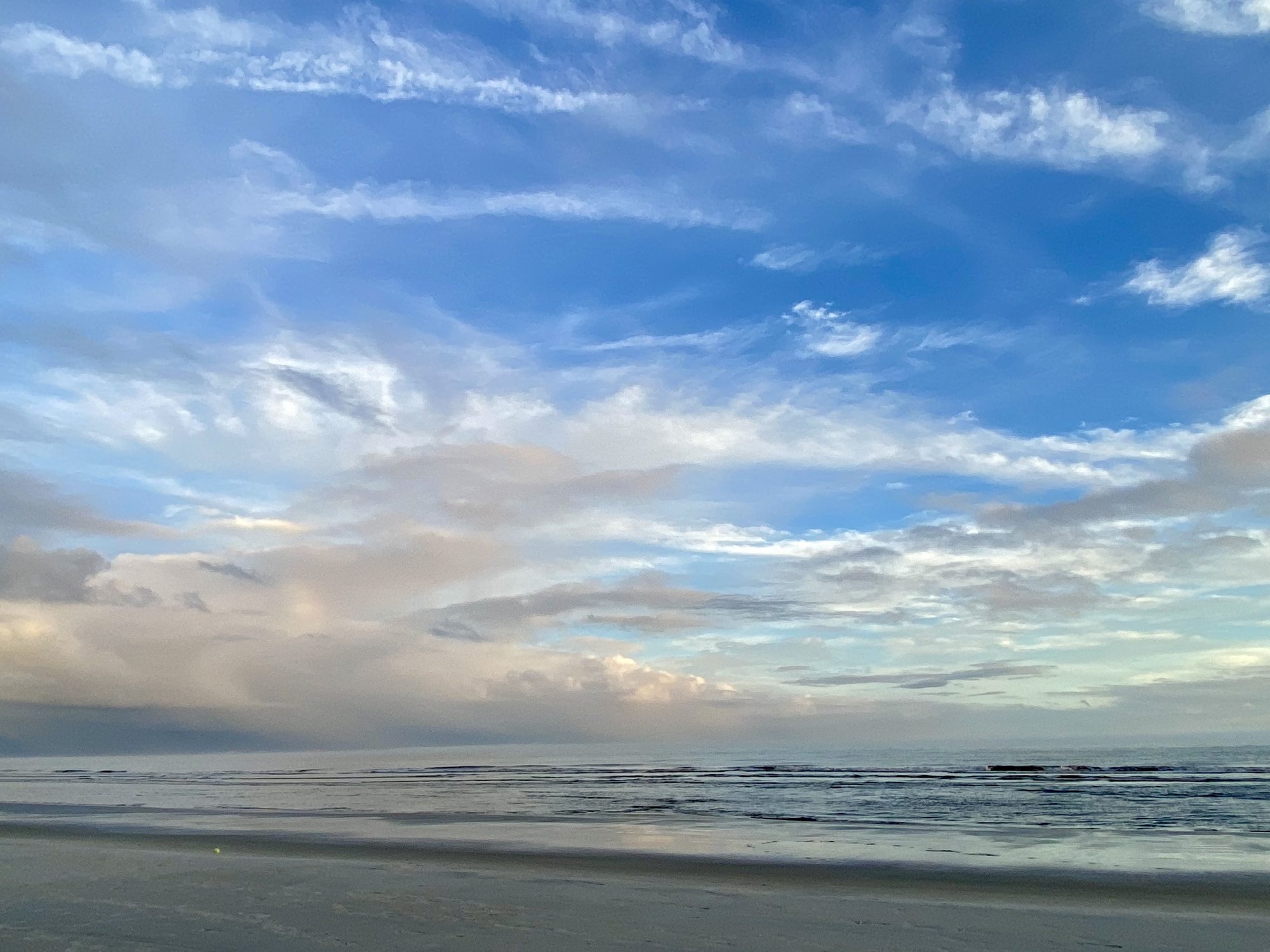 Sky and cloud reflected in a flat sheet of water on the beach.