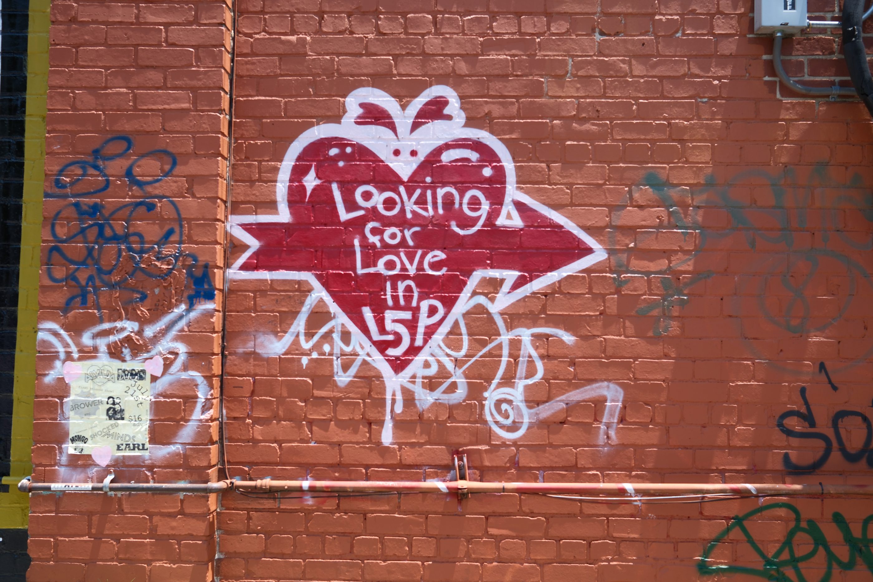 A dark red heart painted on an orange brick wall, lettered 'Looking for Love in L5P'.